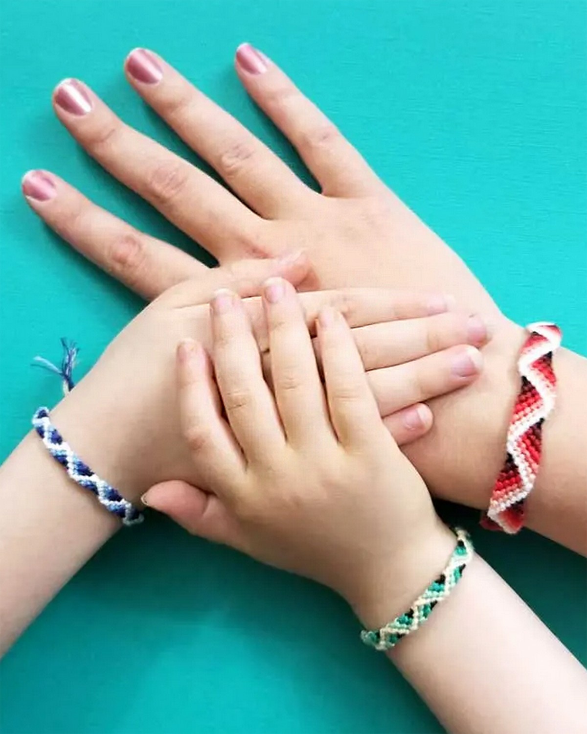 Na obrázku sú destké rúčky a ruka matky s pletenými náramkami priateľstva. 